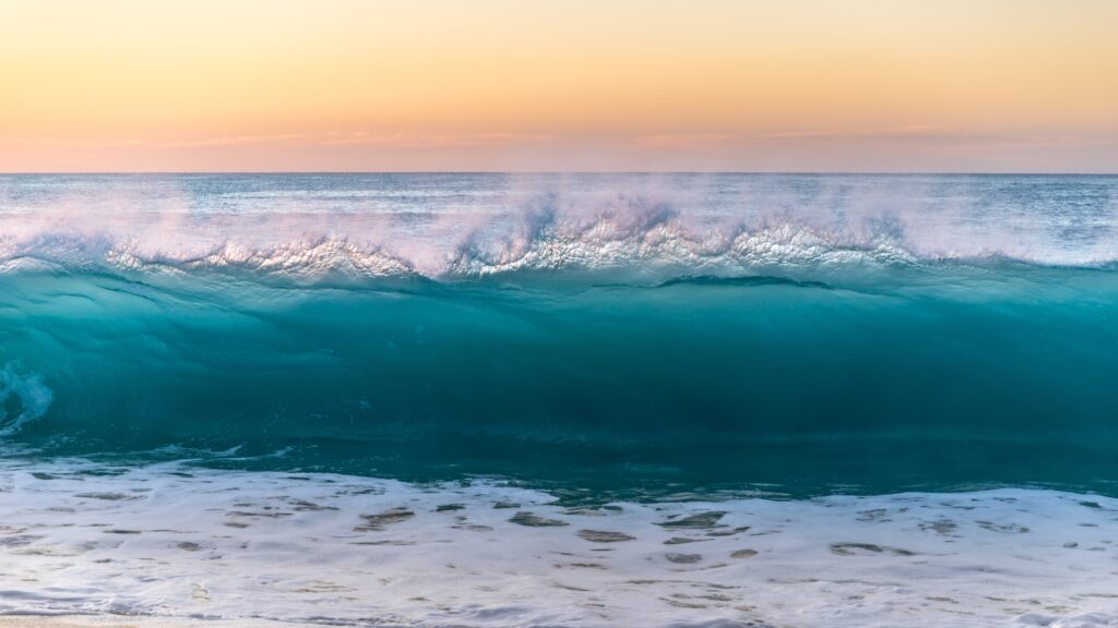 Powerful turquoise wave with foamy spray and mist at sunset ocean wallpaper background