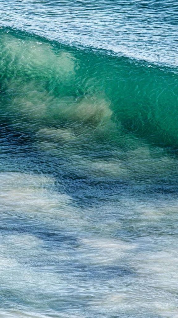 Crashing turquoise ocean wave with translucent foamy crest iPhone wallpaper background serene