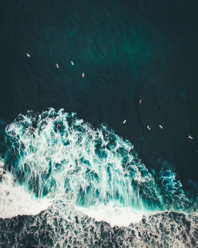 Aerial view of turquoise waves crashing on shore with surfers in deep blue tropical ocean wallpaper
