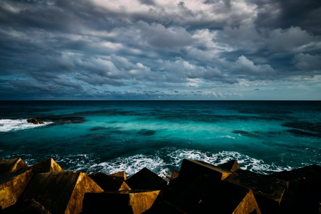 Vivid ocean wallpaper with turquoise waves crashing on rugged coast under layered cloudy sky