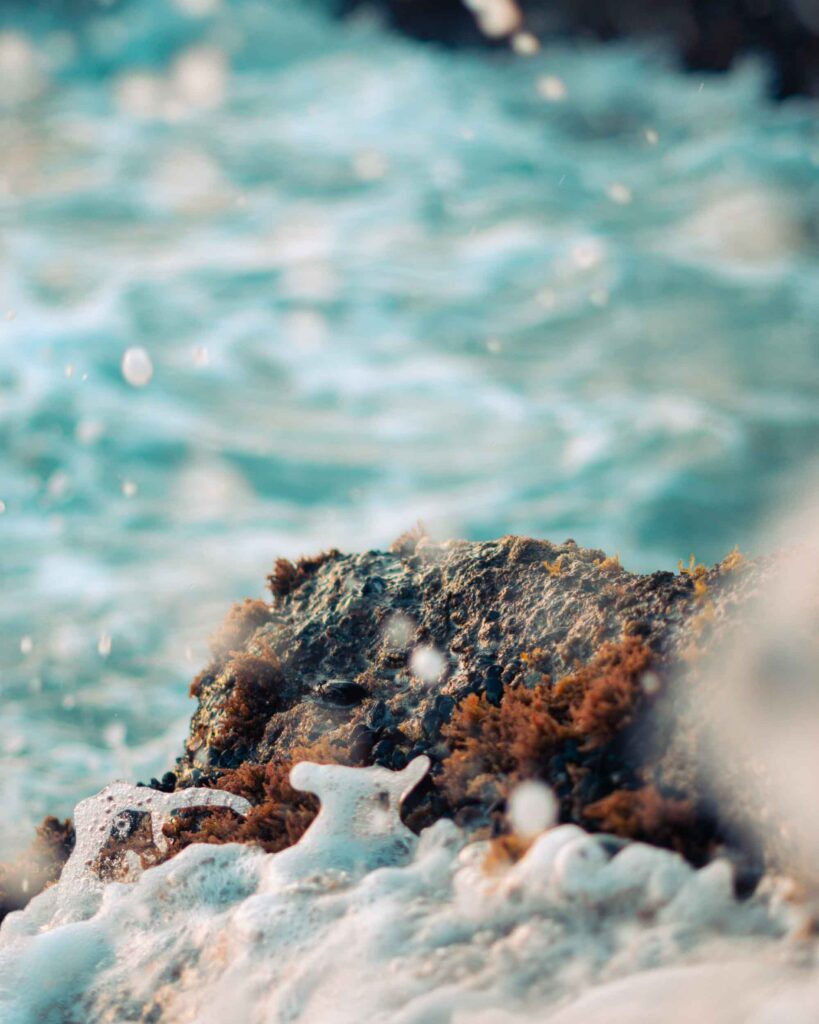 Close-up ocean waves crashing on rugged rock with turquoise foam creating dynamic texture Wallpaper