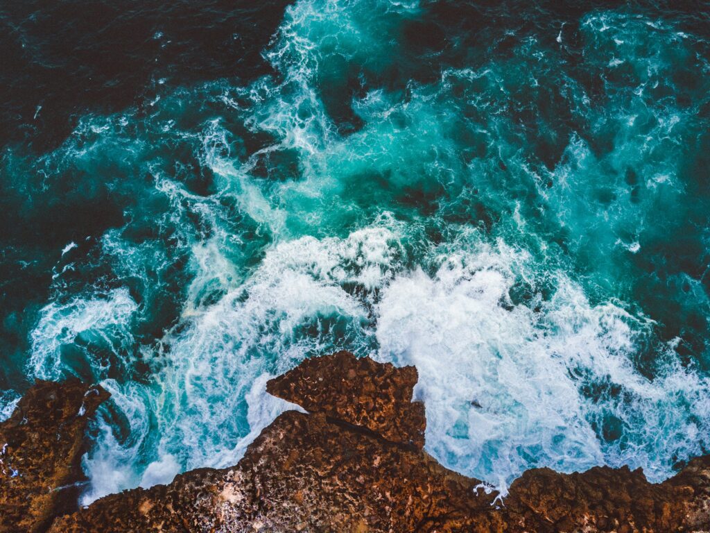 Aerial view of turquoise sea crashing white foamy waves on rugged rocky coastline wallpaper background