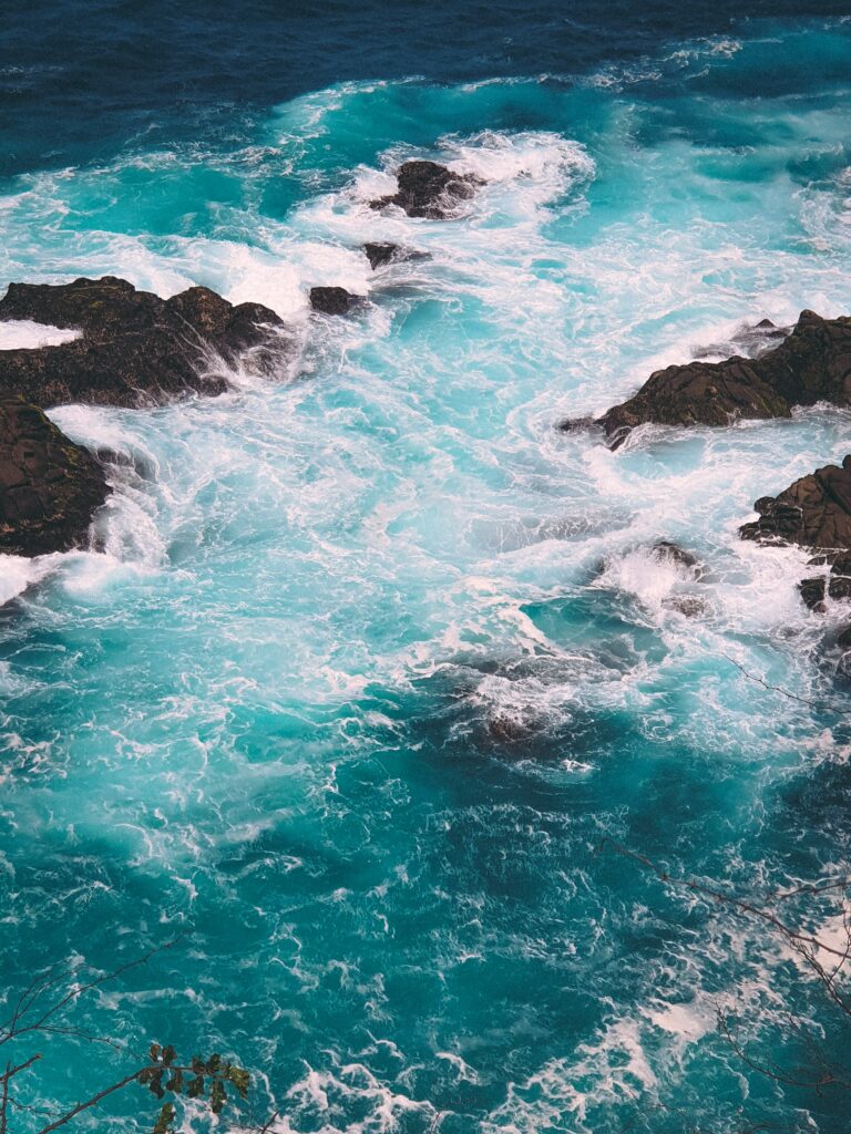 Turquoise ocean waves crashing on rocky shore creating white foam patterns wallpaper background