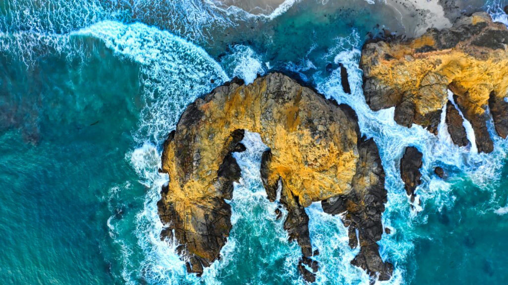 Aerial view of rugged rocks with turquoise ocean waves crashing on shore vibrant coastline wallpaper