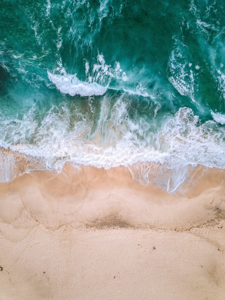 Aerial view of turquoise ocean waves crashing on soft sandy shore with white foam patterns Wallpaper