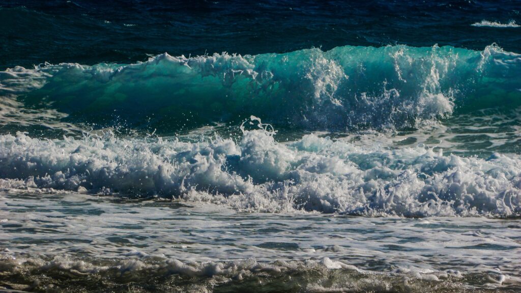 Dynamic turquoise and deep blue sea waves crashing on sandy beach under clear daylight wallpaper