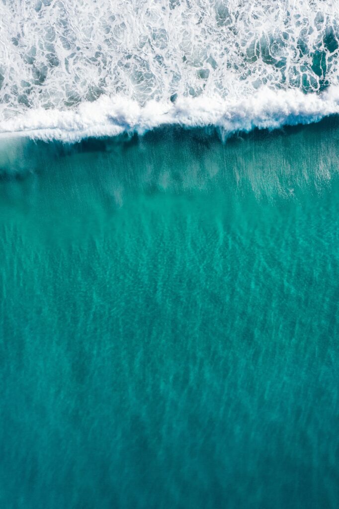 Aerial view of turquoise sea with foamy waves crashing on shore ocean wallpaper background
