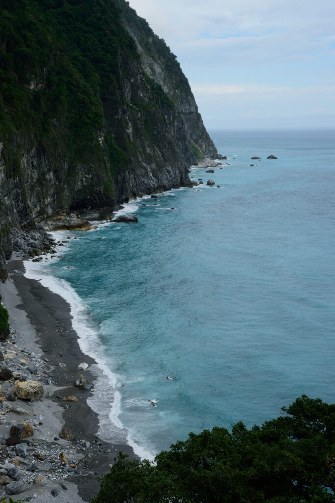Coastal landscape with turquoise waves and lush green cliffs on rocky shoreline wallpaper background