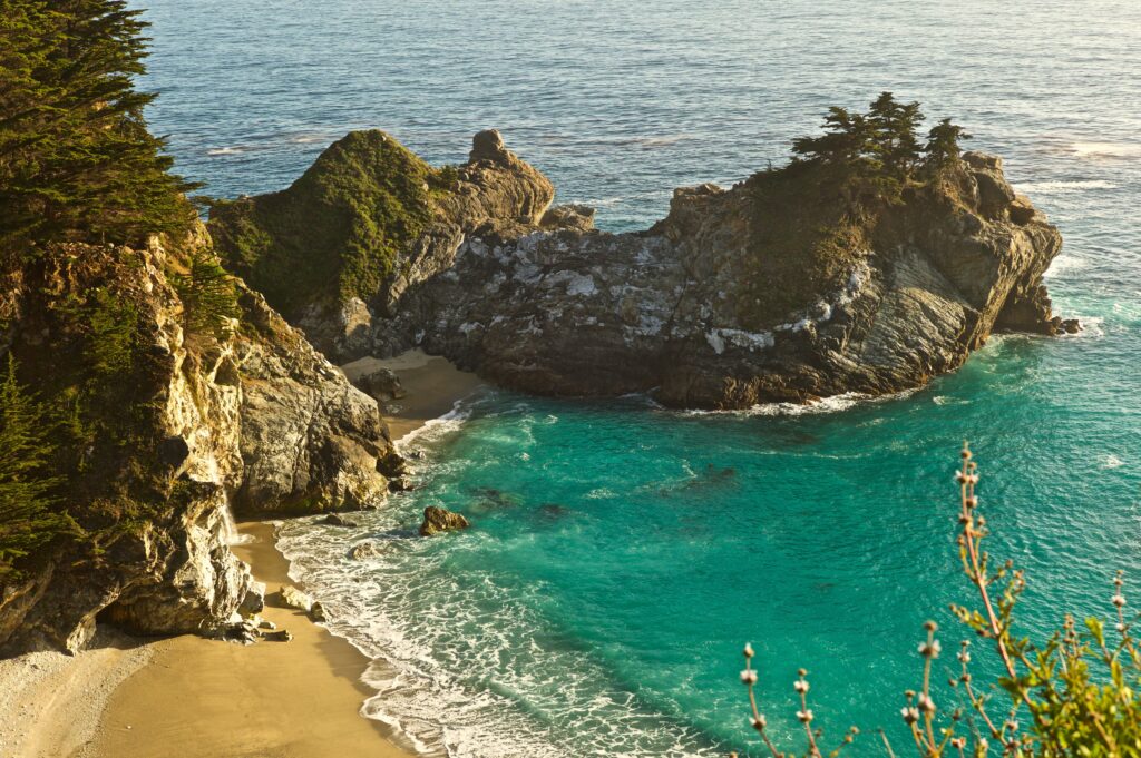 Rugged rock formations and sandy beach with turquoise ocean waves and lush greenery bay wallpaper