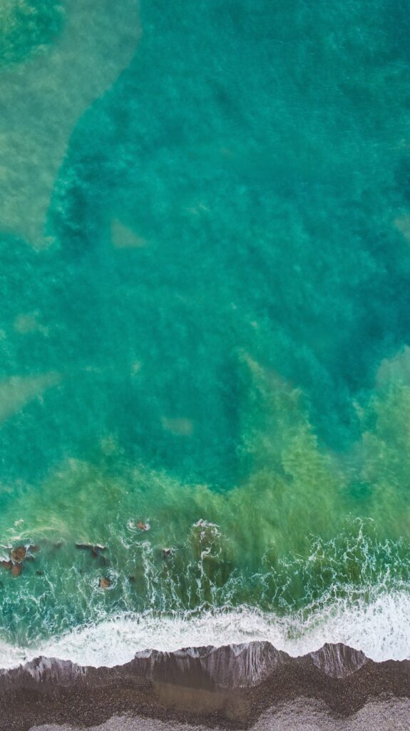 Aerial view of turquoise ocean waves meeting textured coastline for serene wallpaper background