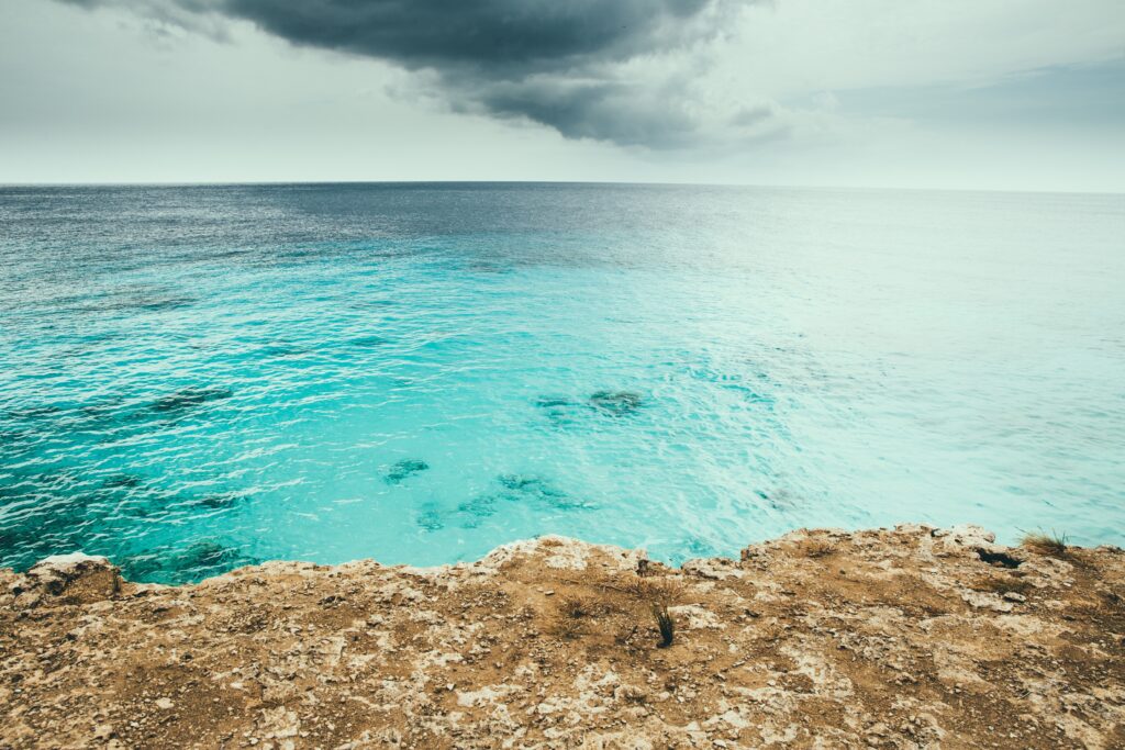 Turquoise ocean waves crashing on rocky shore beneath dramatic cloudy sky coastal wallpaper background