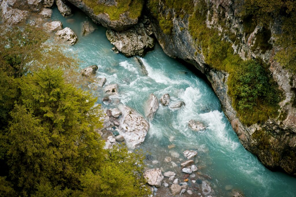 Aerial view of turquoise river winding through rugged rocks and lush green forest landscape wallpaper