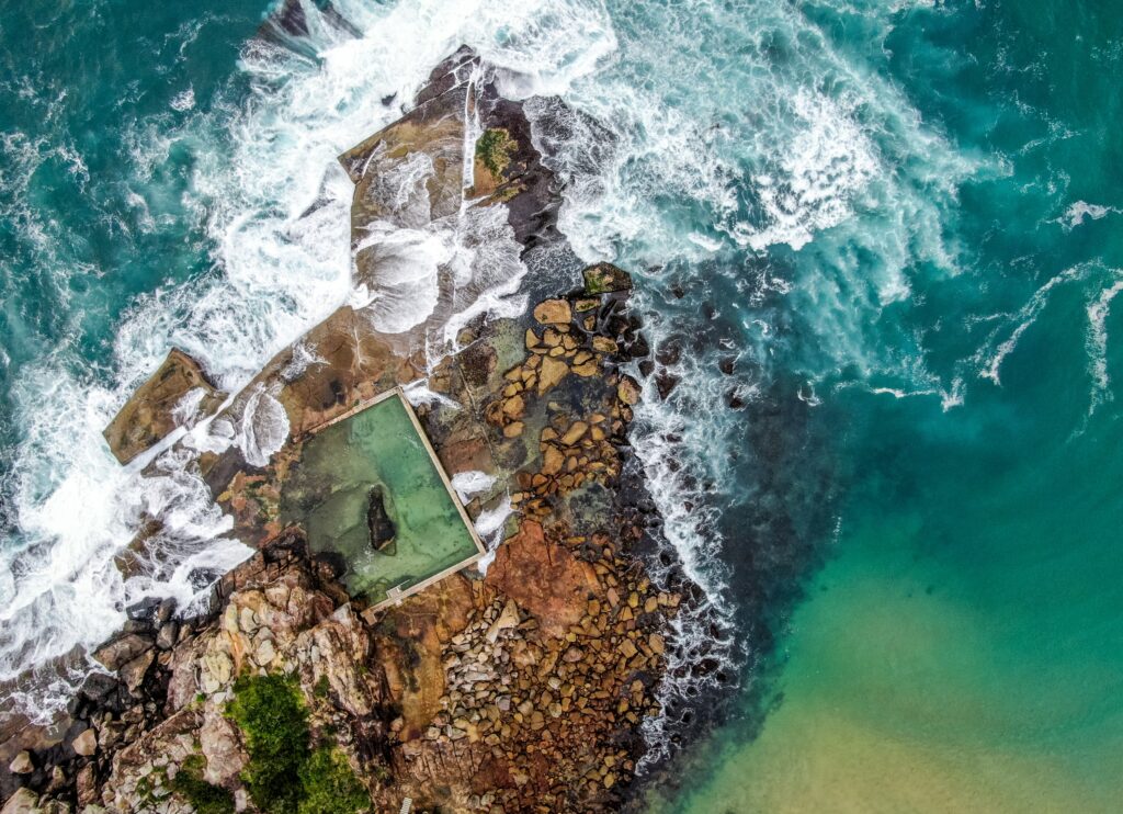 Aerial view of rugged rocks and turquoise sea with foamy waves crashing on rocky coast wallpaper