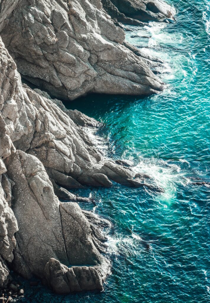 Rugged rocks and turquoise sea with foamy waves crashing on rocky coastline wallpaper background