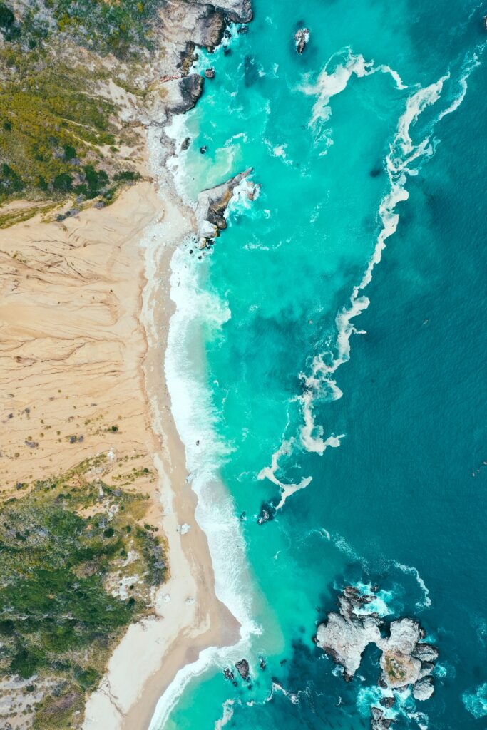 Aerial view of turquoise sea meeting sandy coast with waves crashing rocky beach landscape Wallpaper