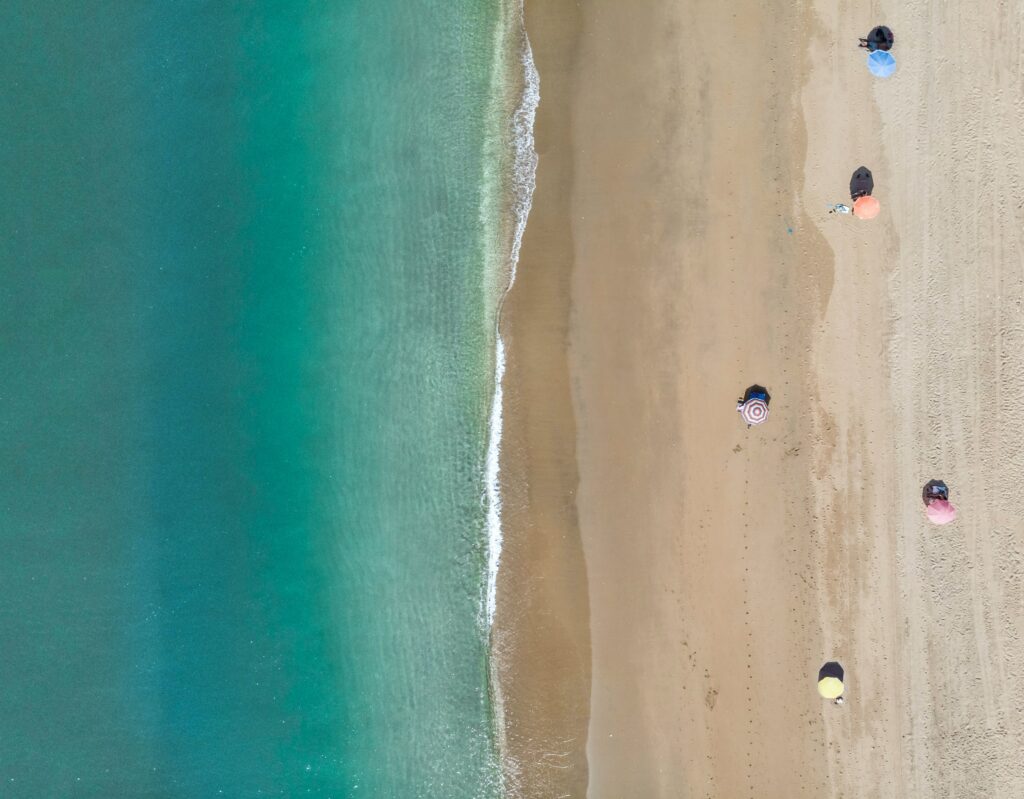 Aerial view of turquoise sea meeting golden sandy beach with colorful umbrellas and footprints Wallpaper