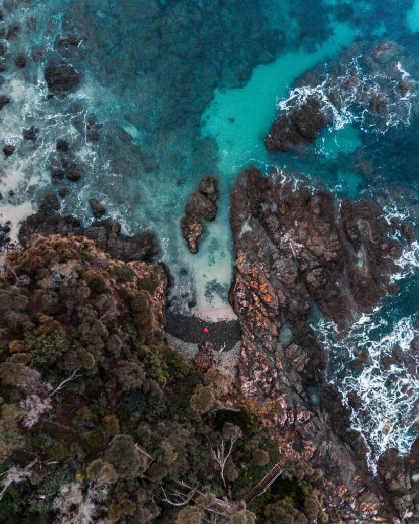 Aerial view of rugged rocky shore meeting turquoise sea with lush green vegetation wallpaper background