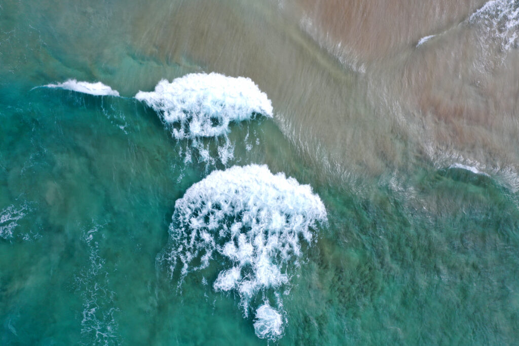 Aerial view of turquoise sea waves gently rolling onto sandy shore with vibrant coastal textures Wallpaper