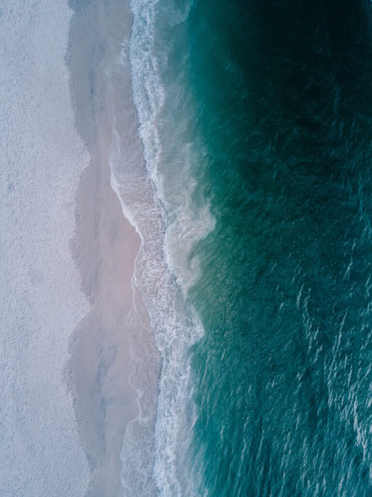 Aerial view of turquoise sea meeting sandy beach with foamy waves coastal landscape wallpaper