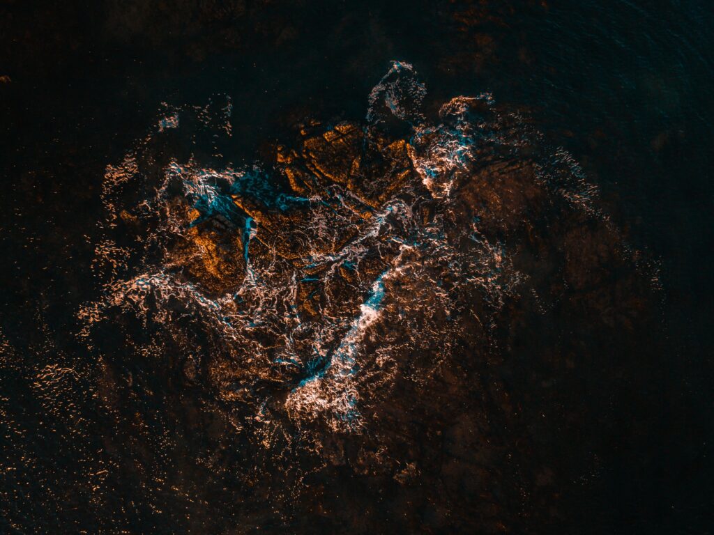 Aerial view of turquoise sea waves crashing on sunlit rugged rocks dramatic natural seascape Wallpaper