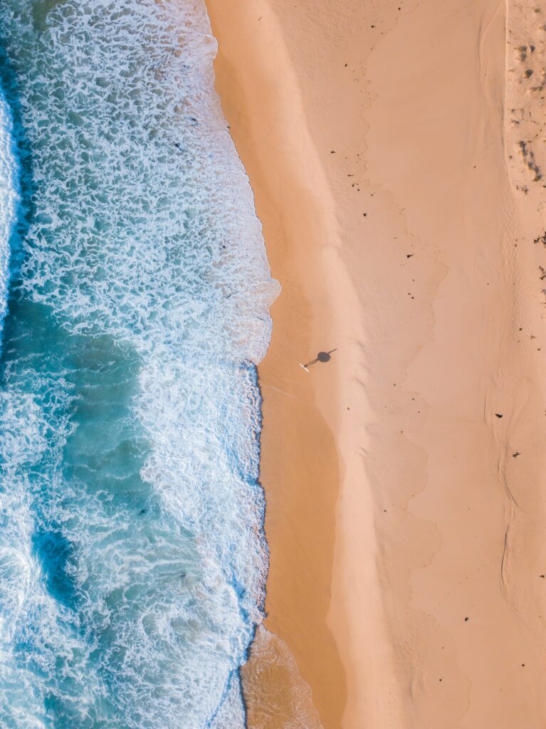 Aerial view of turquoise sea waves gently rolling onto smooth golden sand beach shoreline Wallpaper