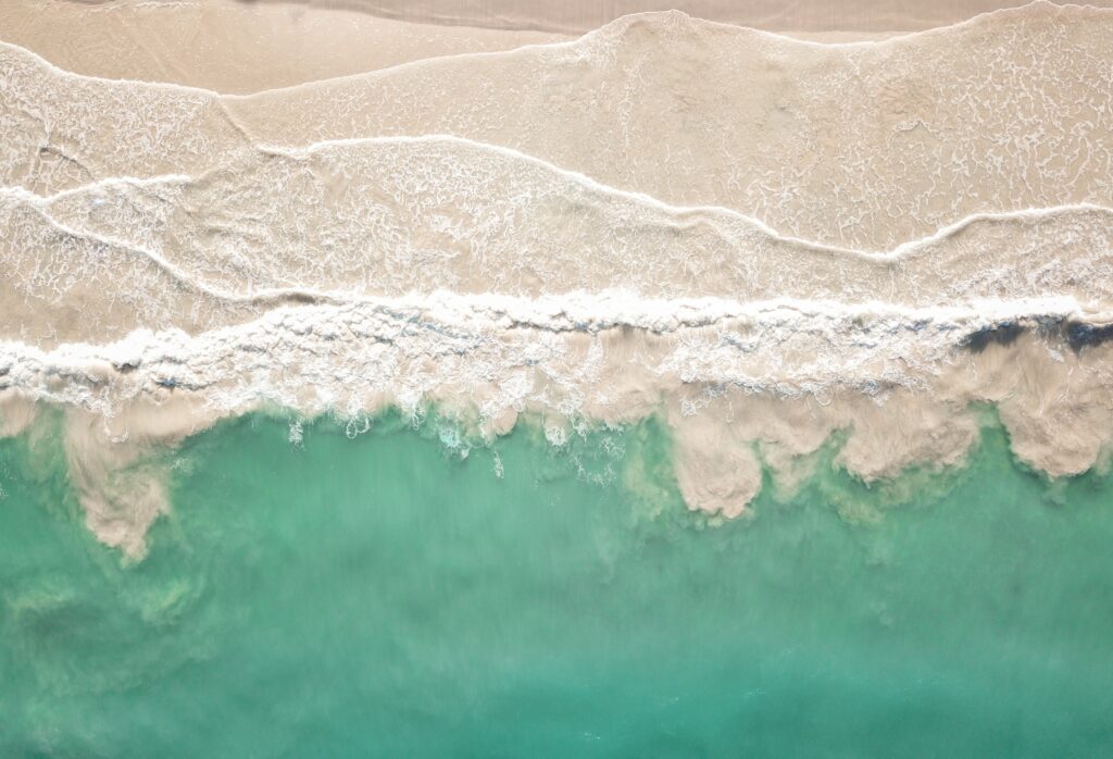 Aerial view of turquoise waves gently meeting sandy beach with natural foam patterns wallpaper