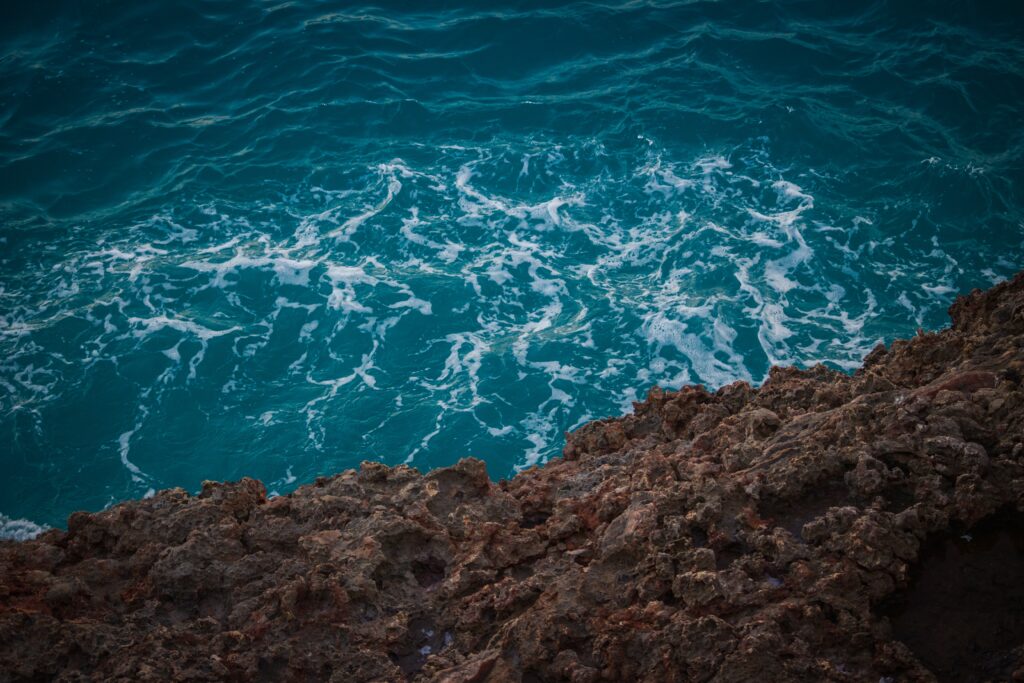 Vivid turquoise sea with white foam and rugged brown stones on a dynamic shoreline wallpaper