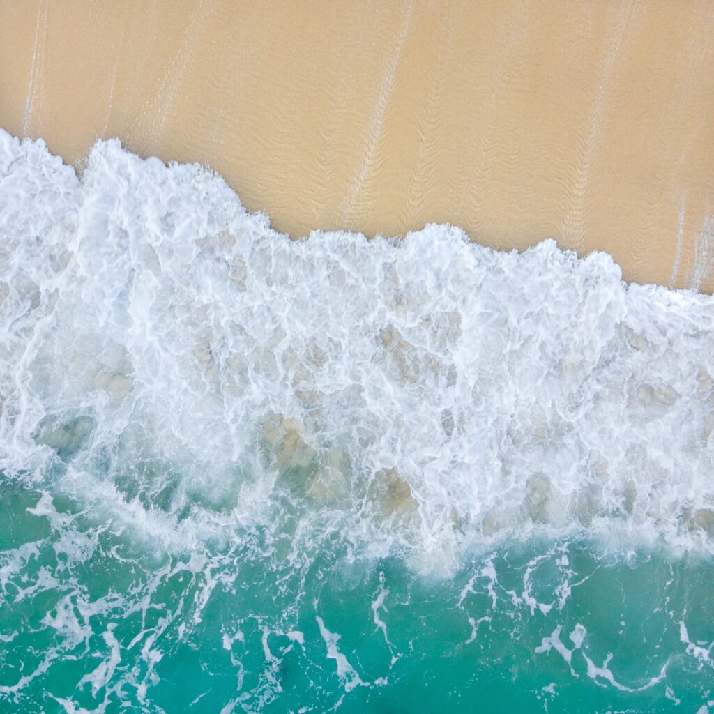 Aerial view of turquoise sea meeting golden sandy beach with gentle white waves rolling ashore Wallpaper