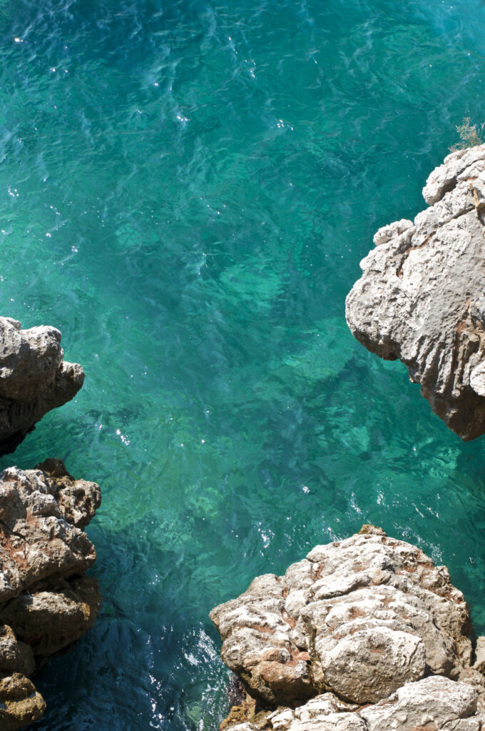 Turquoise sea water with rocky cliffs and weathered stones coastal landscape wallpaper background