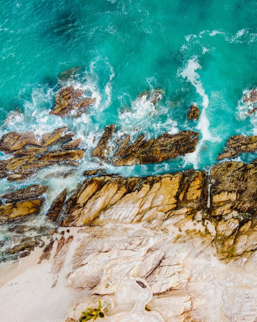 Aerial view of rugged rocks and turquoise sea with foamy waves on a peaceful coastline wallpaper