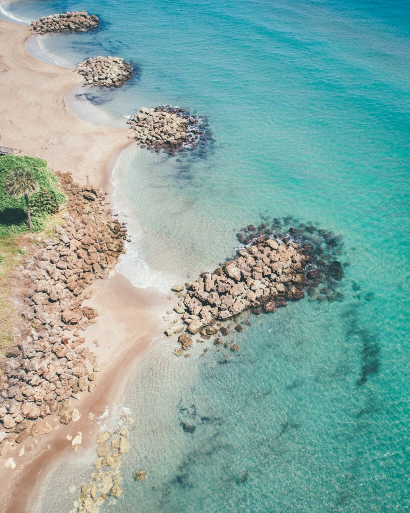 Aerial view of turquoise sea and sandy beach with natural stone formations and gentle waves Wallpaper