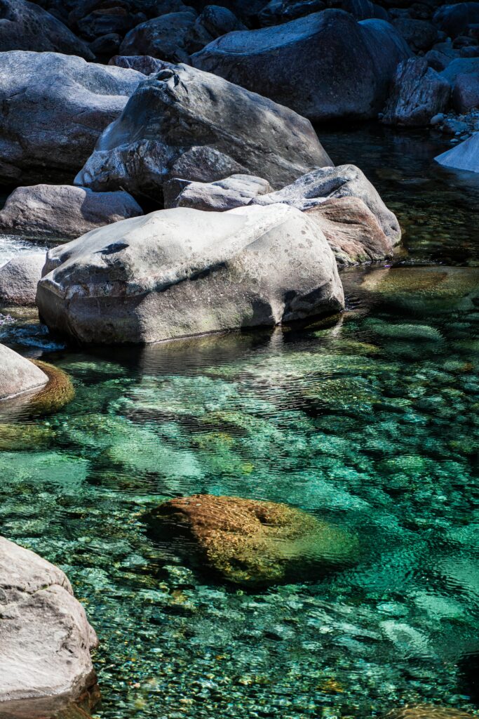 Smooth stones on clear turquoise shore with vibrant reflections and visible pebbles wallpaper