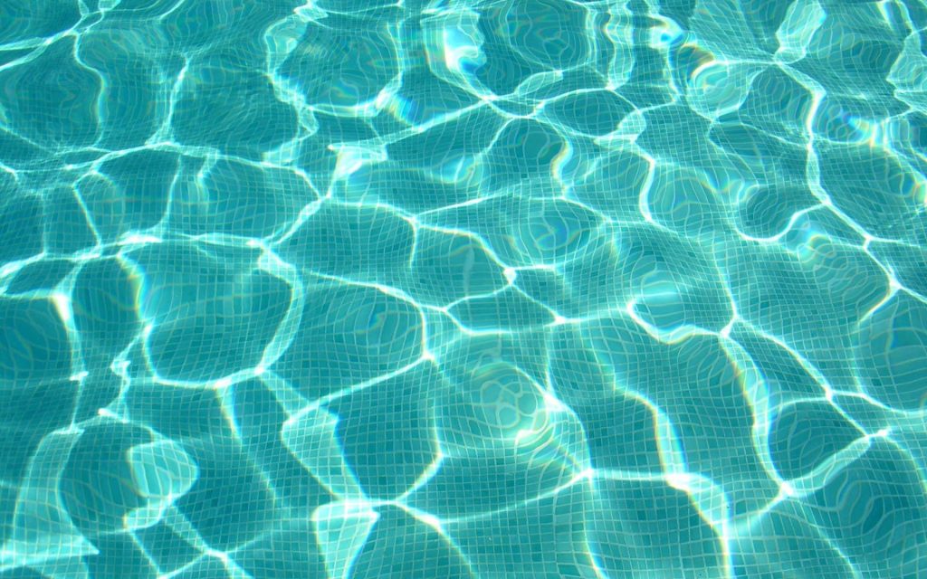 Crystal clear turquoise pool water with sunlit caustic light on blue mosaic tiles wallpaper