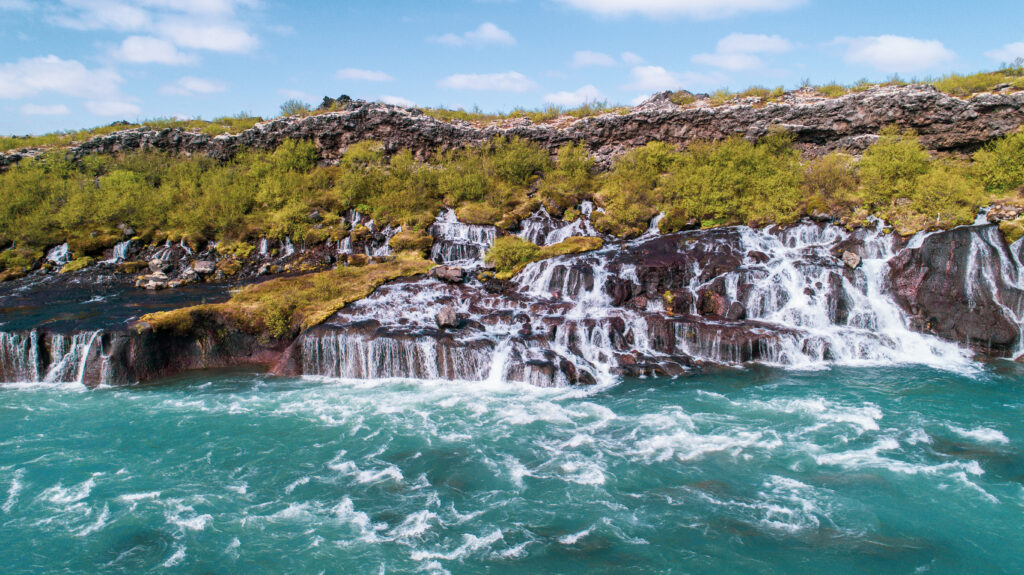 Turquoise waterfalls cascading rocky cliffs with foamy streams and lush green bushes background Wallpaper