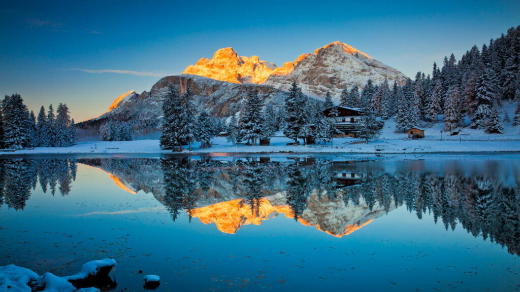 Winter Dolomites Lake Misurina with golden alpenglow snow peaks and cozy cabin reflection Wallpaper