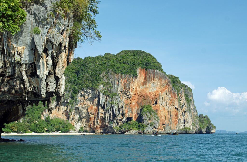 Serene tropical seascape with turquoise waters limestone cliffs lush greenery and anchored boats Wallpaper