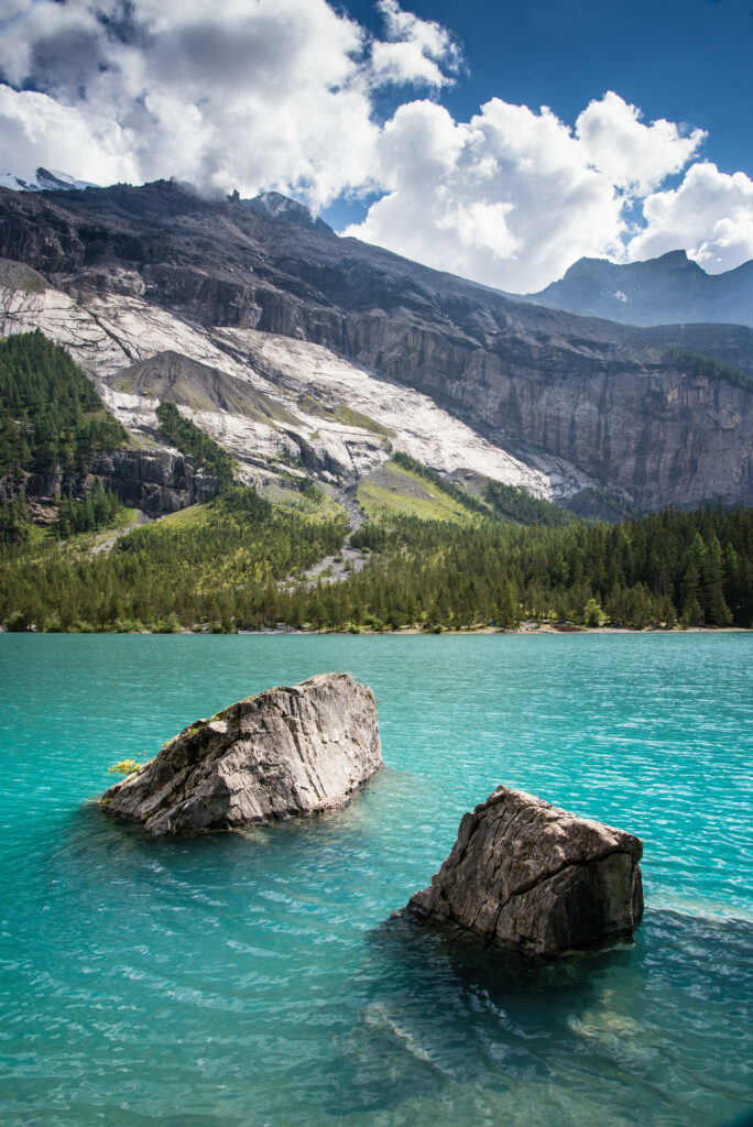 Two large stones rise from turquoise waters with green forests and rocky mountains background Wallpaper