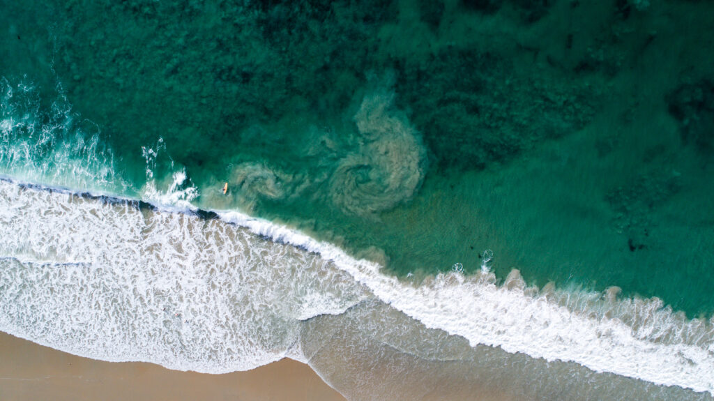 Aerial view of turquoise waves and sandy beach with foamy patterns in a vibrant summer scene Wallpaper