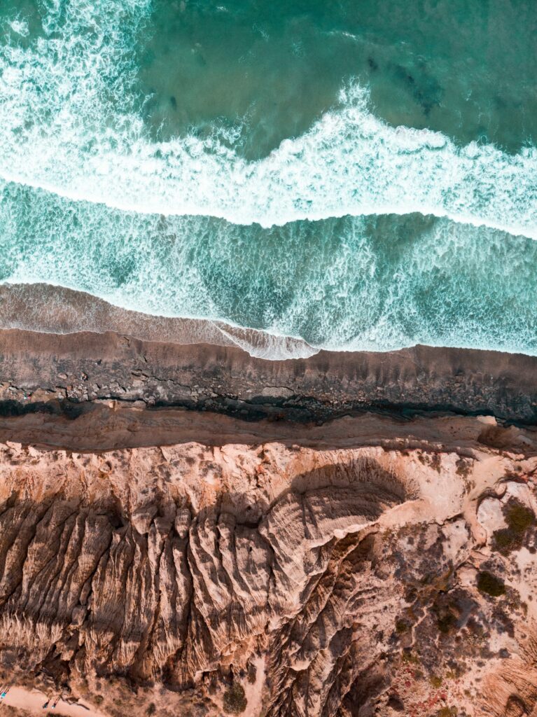 Aerial view of rugged coastline with turquoise waves crashing on dramatic rocky cliffs wallpaper