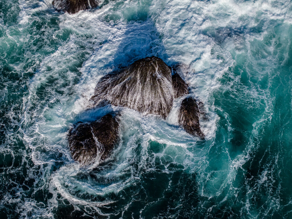 Aerial view of turquoise ocean waves crashing on dark rocks with white foam patterns wallpaper