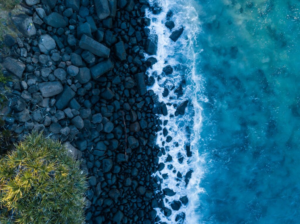 Aerial view of turquoise ocean waves crashing on dark rocky coastline with lush green shore wallpaper