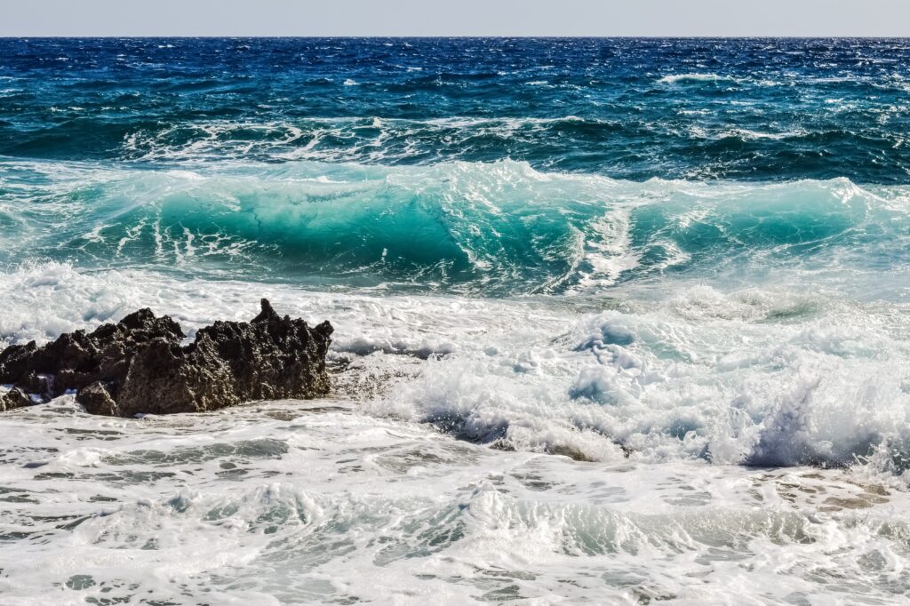 Turquoise waves crash on rugged rocks with foamy surf and dynamic blue textured coastline Wallpaper