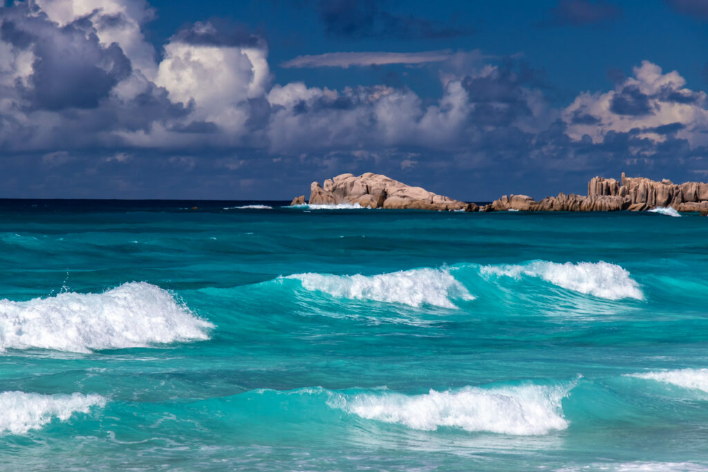 Turquoise waves crash on rugged rocks under dramatic cloudy sky seascape wallpaper background