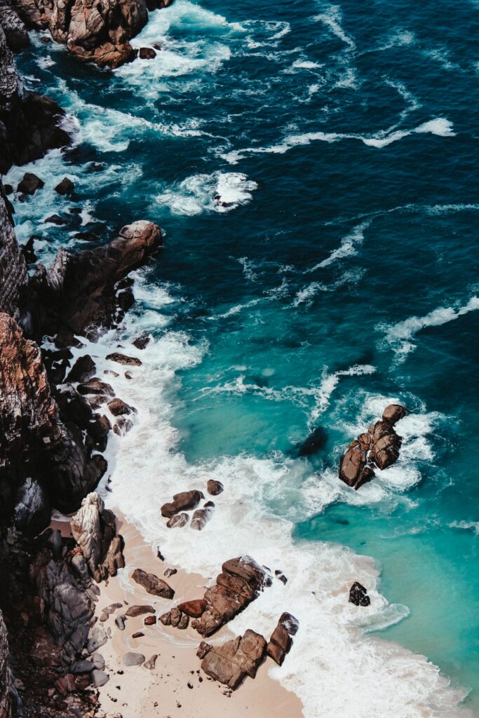 Aerial view of turquoise waves crashing on rocky cliffs and sandy beach coastline wallpaper