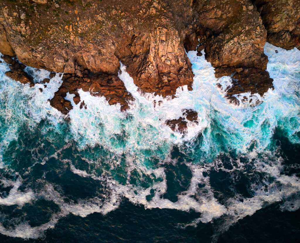 Aerial view of rugged rocky shore with turquoise waves crashing and foamy white surf wallpaper