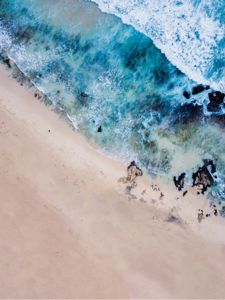 Aerial view of serene turquoise waves meeting sandy shore with rocks and soft foam beach wallpaper