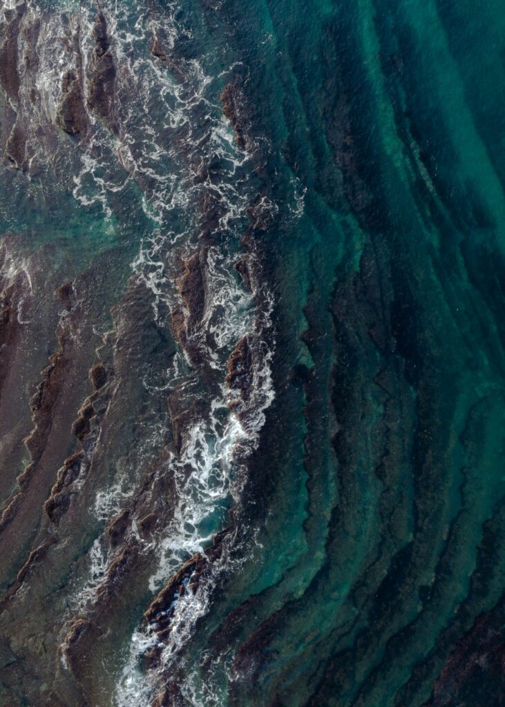 Aerial view of turquoise waves flowing over submerged rocks with earthy tones and textures Wallpaper