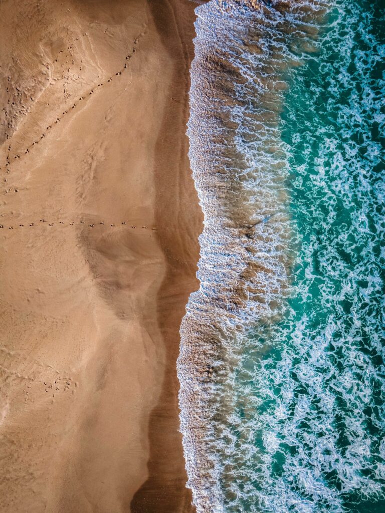 Aerial view of turquoise waves meeting golden sand with footprints on a tranquil beach wallpaper