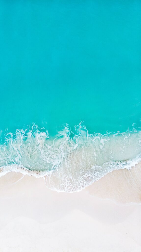 Aerial view of turquoise waves gently washing onto a pristine sandy beach wallpaper background