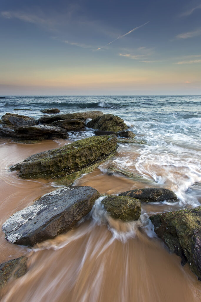 Twilight beach with mossy stones gentle sea tides pastel sky and deep blue ocean horizon wallpaper